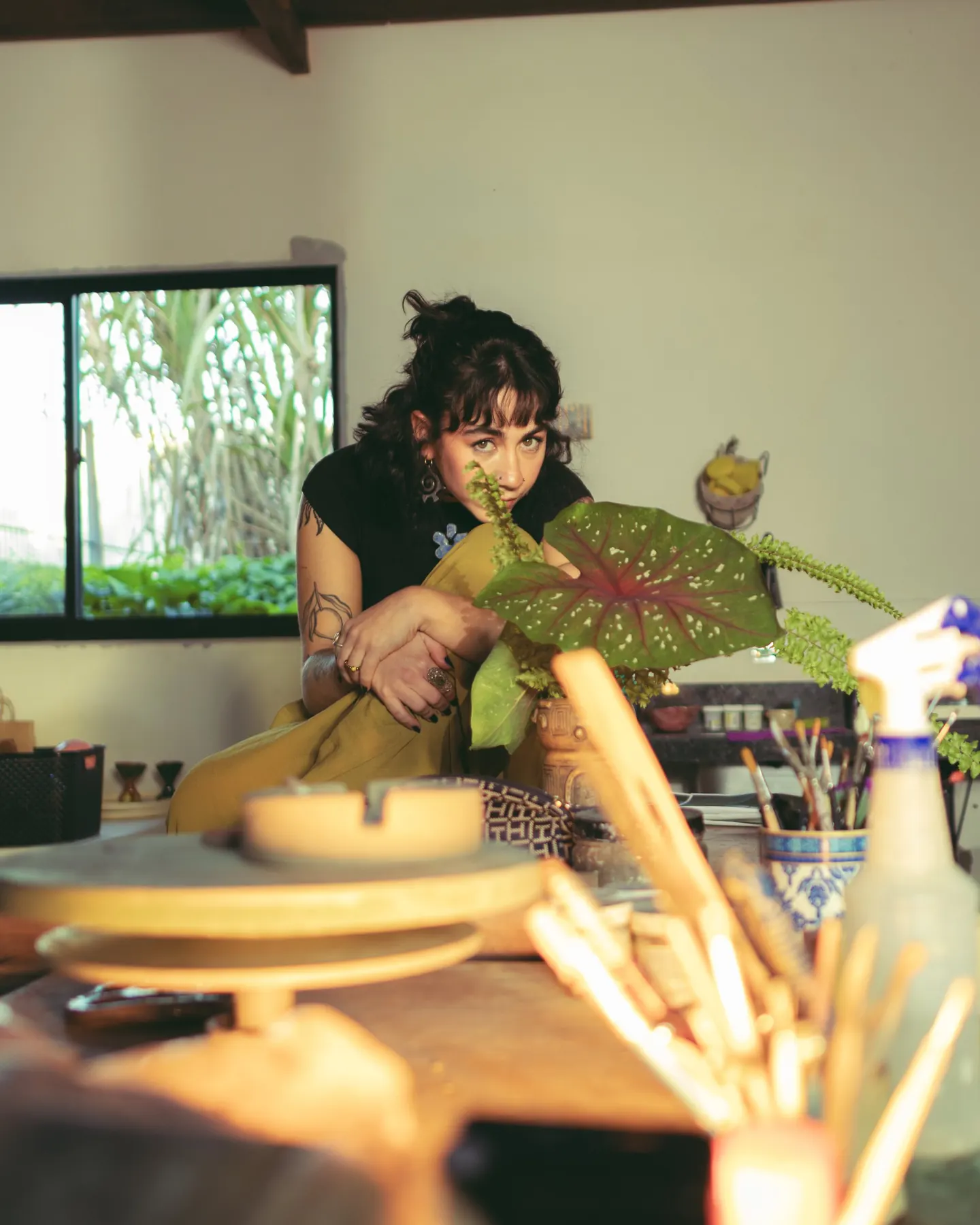 Ceramista sentada no ateliê, entre plantas e ferramentas