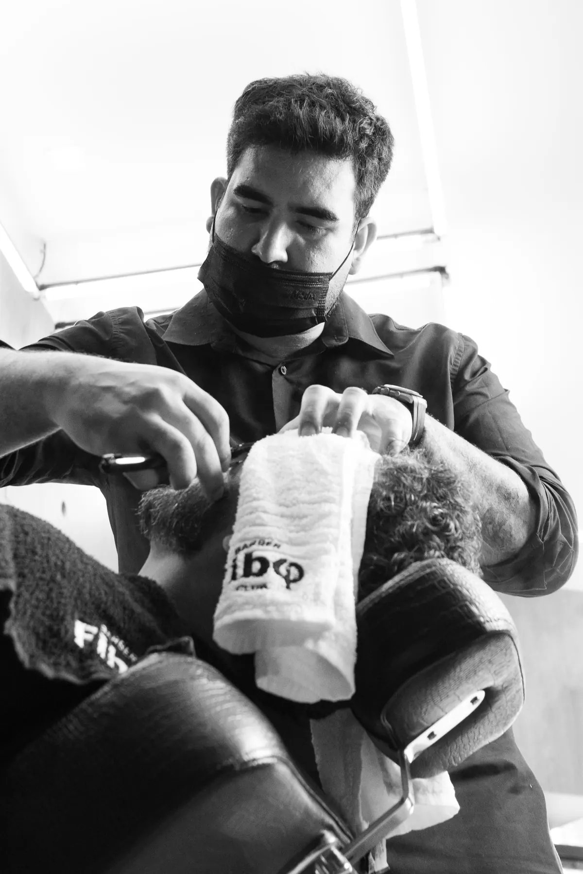 Barbeiro fazendo a barba de um cliente na Fibo Barbearia